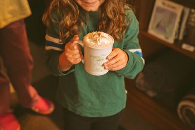 Enfant tenant une tasse de chocolat chaud garnie de crème fouettée